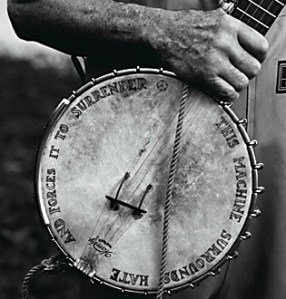 Pete grips his banjo. The words on the banjo read; "This machine surrounds hate and
