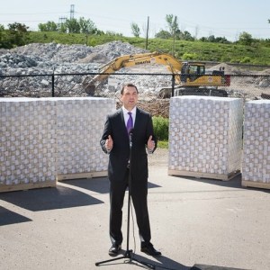 Ontario Tory Leader Tim Hudak at recent photo op, with skids of fake Canadian dollars behind him, at rejected Mississauga gas plant site. 