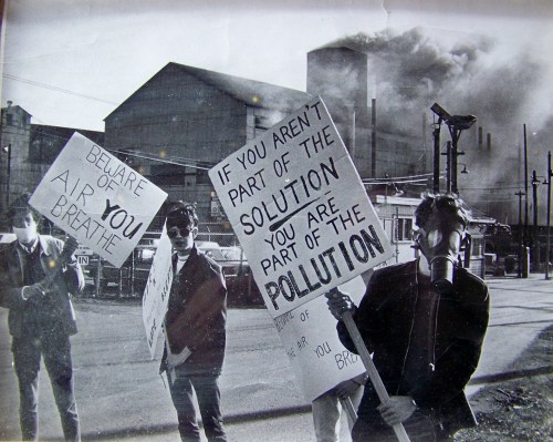 Niagara At Large publisher and environment reporter Doug Draper with the gas mask and "If you are not part of the solution" sign, demonstrating in front of a then polluting Union Carbide plant in Welland, Ontario on the first Earth Day, April 22, 1970.