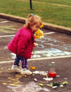 At the 25th commemoration ceremonies in 1995 for the 1970 Kent State shootings, a little girl places flowers on a spot where one of four students fell dead. Photo by Doug Draper